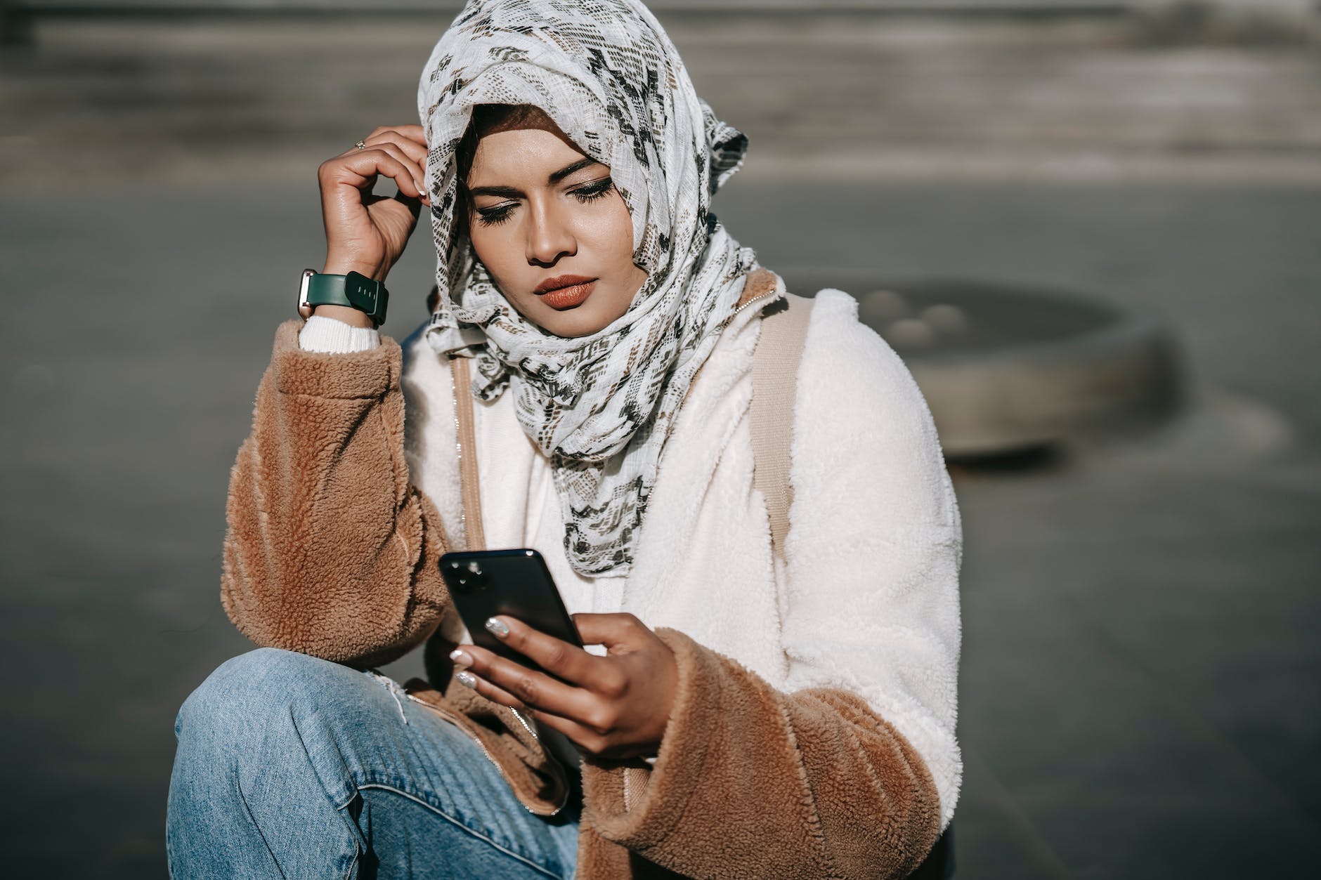 stylish young ethnic lady in hijab using mobile phone on street